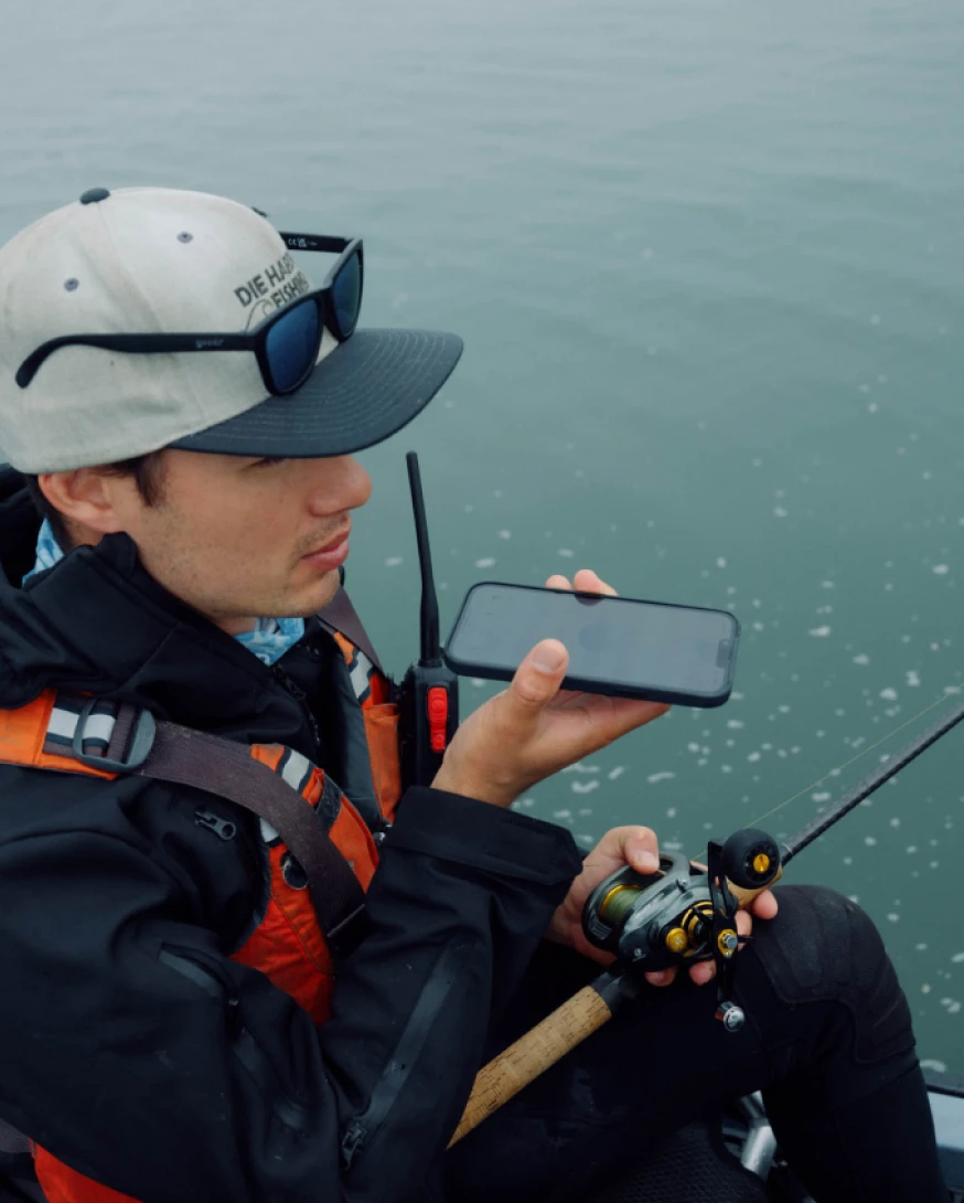 Fisher using ChatGPT on a smartphone for halibut fishing tips on a boat